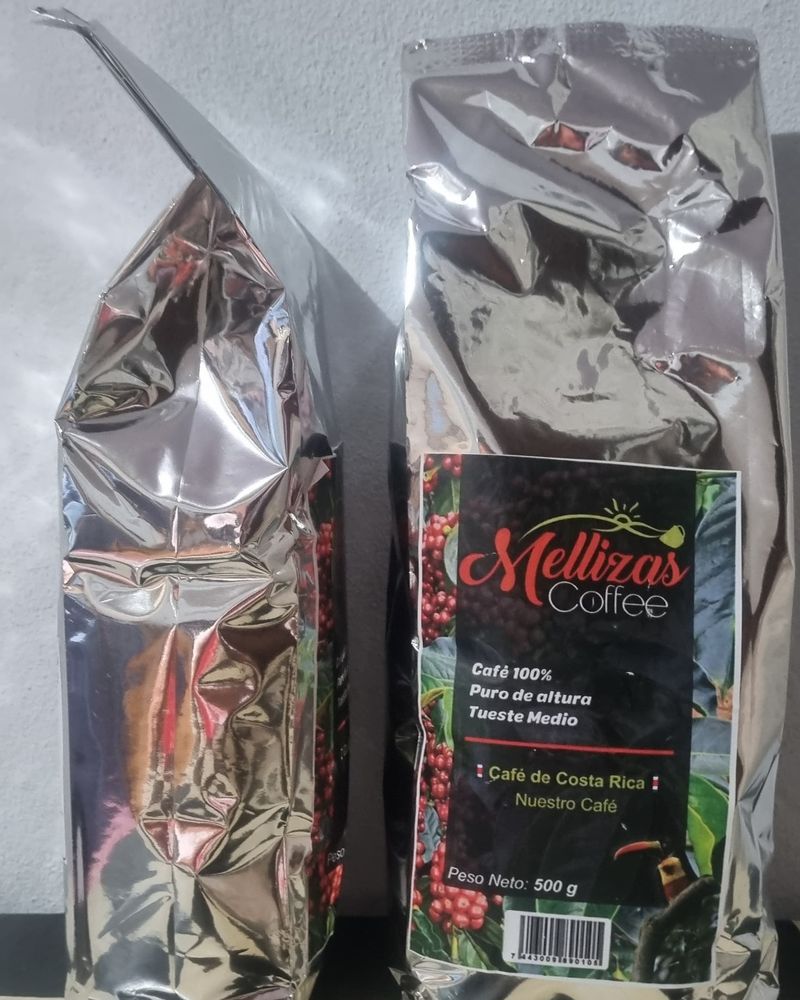 Una bolsa plateada de 500 g de Mellizas Coffee vista de lado junto a otra de frente con la etiqueta a color, sobre un piso de cuadros