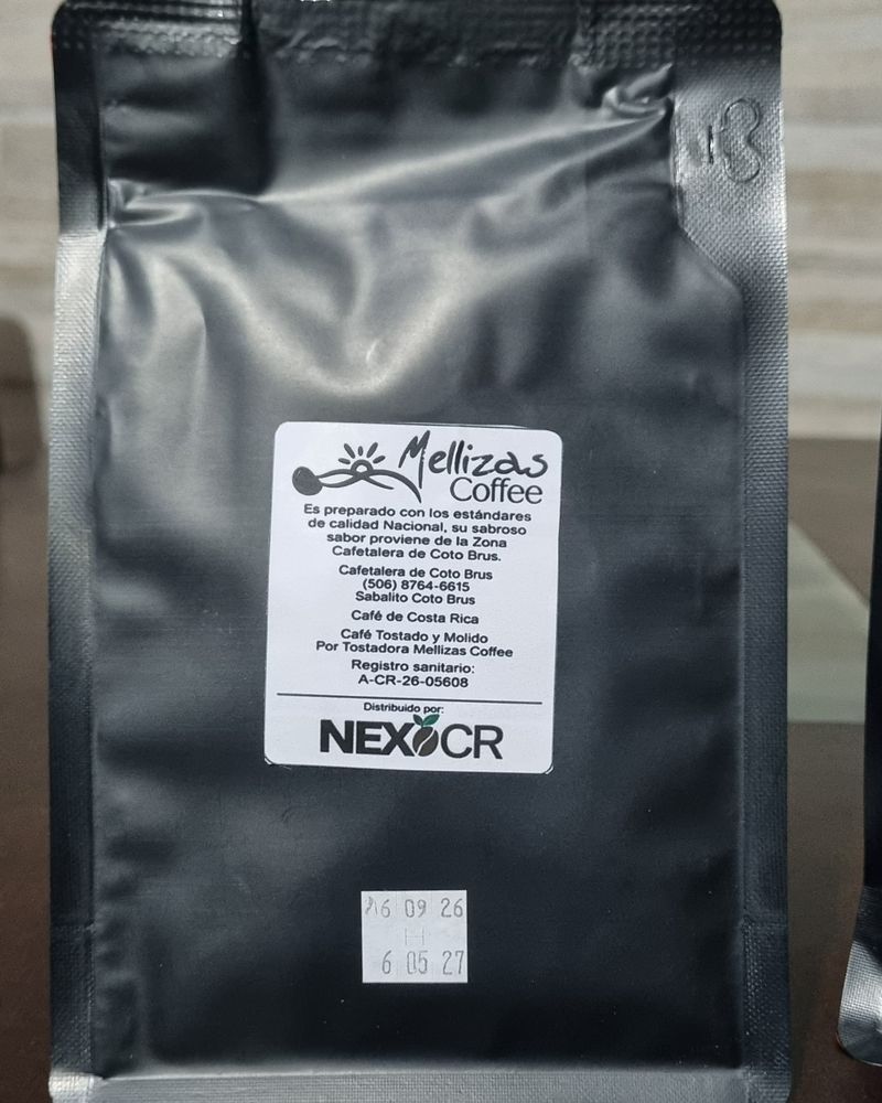 Parte trasera de una bolsa negra de 250 g con la etiqueta blanca de Mellizas Coffee: datos de la cafetalera, registro sanitario A-CR-26-05608 y el texto Distribuido por Nexo CR